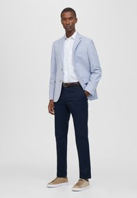 Blazer a rayas azul claro, camisa blanca, pantalones navy y zapatillas beige. El blazer presenta botones dorados y un detalle de bolsillo. Textura suave.