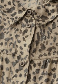 Beige shirt with a leopard print pattern, featuring a collared neckline, two buttons, and subtle stitching detail along the seam.
