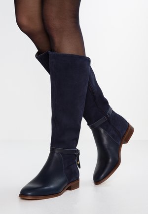 Bottes en daim et cuir bleu marine jusqu'au genou, présentant un design ajusté, une fermeture éclair sur le côté et un petit talon en bois robuste.