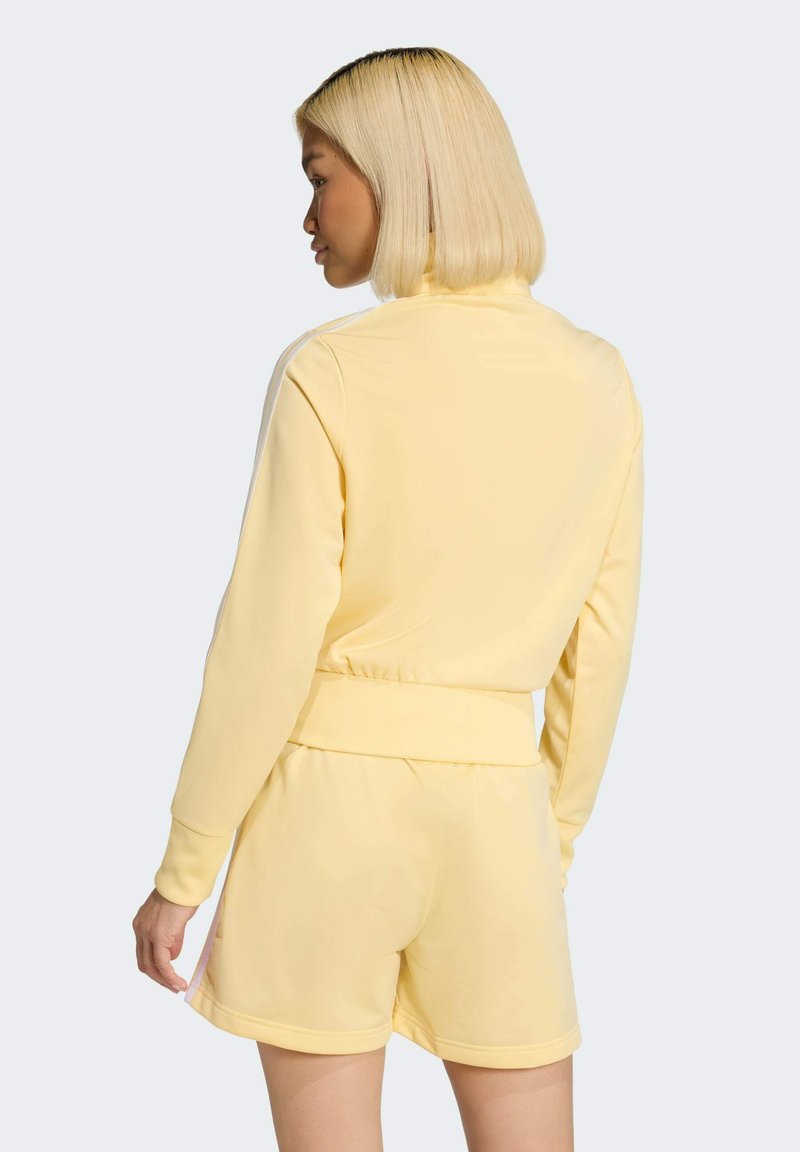 Yellow tracksuit top with a high collar, ribbed cuffs, and matching shorts. Smooth fabric with subtle stretch; features white side stripes.