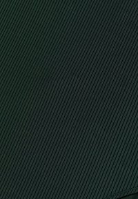 Mörkgrön texturerad tyg med vertikal ribbad mönster, vilket ger en taktil yta med synliga sömdetaljer längs kanterna.