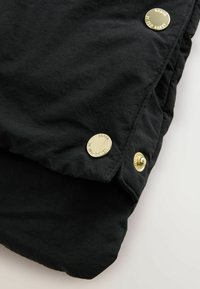 Tessuto nero con una leggera texture stropicciata, caratterizzato da bottoni a pressione dorati e dettagli di cucitura, che mostra una vista ravvicinata del capo.