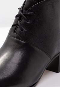 Zapato de cuero negro con acabado texturizado, punta redonda y tacón bajo cuadrado. Presenta un diseño de cordones con agujetas negras a juego.