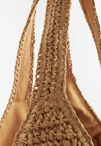 Spleciona torba z słomy z teksturowanymi, jasnobrązowymi uchwytami i gładką podszewką, z misternym plecionym wzorem i detalami szycia.
