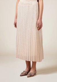 Gonna midi plissettata in beige chiaro con una finitura lucida e testurizzata. La vita è elastica e viene abbinata a scarpe a punta con motivo.
