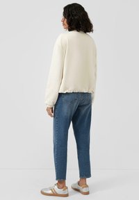 Sweat-shirt beige clair à col rond, poignets et ourlet côtelés, associé à un jean denim bleu ample et des baskets argentées.