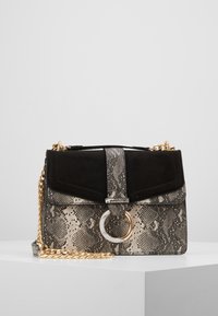 Kabelka s hadím potiskem, která má černou semišovou klopu, kulatou kovovou ozdobu a zlatý řetízek jako popruh. Kompaktní obdélníkový tvar.