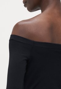 Sorte avtagbart-top med lange ermer, laget av glatt stoff. Har en tettsittende design som fremhever skuldrene og nakken.