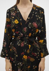 Blommig kimono i svart tyg med V-hals, långa ärmar och ett matchande knyt-bälte. Designen inkluderar flerfärgade blommönster och accenter.