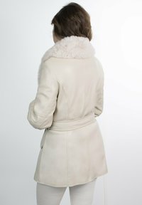 Chaqueta de cuero crema con un suave collar de piel sintética, cintura ceñida, diseño entallado y detalles de costura en la parte posterior.