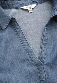 Denim-paita, jossa on V-pääntie, vaaleansininen kangas ja kauluksellinen muotoilu. Labelissa lukee "CELLBES of SWEDEN," koko 38/40. Pehmeä rakenne, rento ilme.