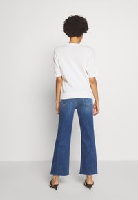 Bílý pletený svetr s krátkými rukávy, kombinovaný s tmavě modrými volnými džíny s vysokým pasem a roztrhanými okraji, a s černými špičatými podpatky.