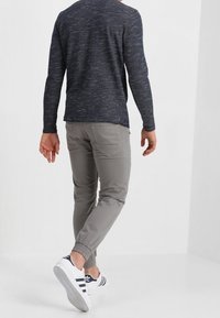 Navyblaues, strukturiertes Langarmhemd, graue, taillierte Hose und weiße Sneakers mit navyblauen Streifen. Einfaches Design mit minimalen Details.