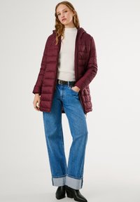 Bordo puf jakna s kapuljačom, u kombinaciji s kremastim rebrastim džemperom, širokim plavim trapericama i crnim čizmama na petu do gležnja.