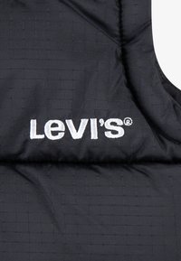 Svart isolerad väst med ett kviltat mönster. Har den vita broderade "Levi's"-logotypen tydligt synlig. Mjuk textur och lätt material.