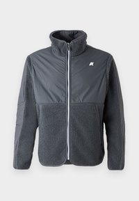 Veste zippée grise avec une texture en polaire sur la moitié inférieure et les manches. Présente un col haut et un petit logo sur la poitrine gauche.