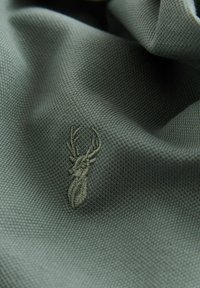 Grönt texturerat tyg med en subtil broderad hjortdesign, som visar på fin detaljrikedom och ett mjukt, vävt material.