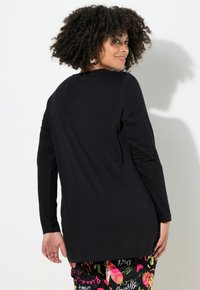 Maglietta nera a maniche lunghe con scollo rotondo, texture liscia e vestibilità ampia, abbinata a pantaloni colorati e a fantasia.