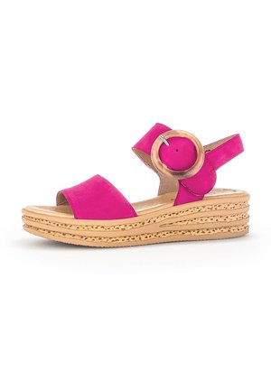 Sandale en suède rose avec une semelle en liège profilée, dotée d'une sangle ajustable et d'un grand accent circulaire en bois sur le côté.