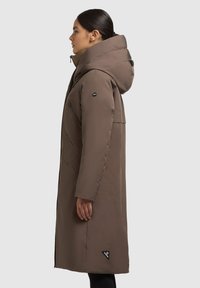 Bruine lange jas met een hoge kraag en capuchon, met een diagonale gestikte ontwerp en logo-accent op de mouw en onder zoom.