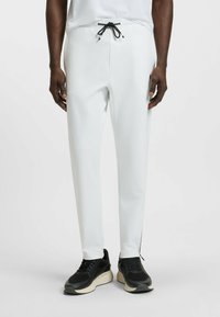 Witte, slim-fit broek met een elastische tailleband en zwarte koord; heeft zijzakken met rits en contrasterende naden. Gepaard met zwarte sneakers.