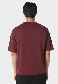 Bordové tričko s krátkým rukávem a kulatým výstřihem, hladká textura a minimální švy na zadní straně.