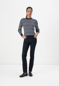 Marine gestreepte trui met witte lijnen, lange mouwen, ronde hals; gecombineerd met donkere slim-fit jeans en zwarte instappers. Eenvoudig, klassiek ontwerp.