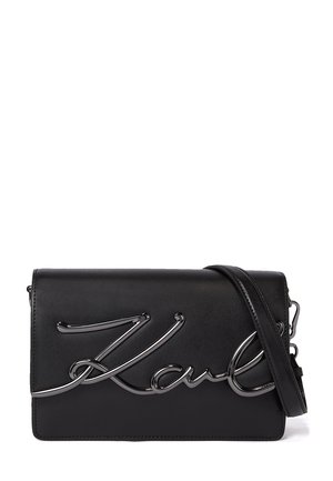 Sac bandoulière rectangulaire en cuir noir avec un logo script en métal argenté sur le devant et une bandoulière réglable.
