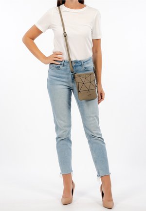 Mujer vestida con una camiseta blanca, jeans de mezclilla de color azul claro, tacones nude y un bolso cruzado beige con un diseño de líneas negras geométricas.