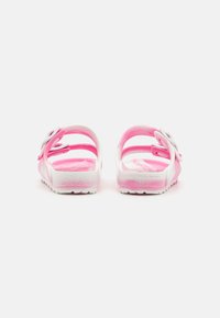 Sandalias rosas y blancas con un diseño floral, hechas de plástico suave, que cuentan con una correa ajustable y una suela texturizada para mayor agarre.