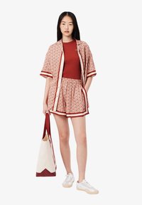 Chemise à manches courtes à motifs rouges et shorts assortis avec des bordures blanches, associés à un haut rouge ajusté et un sac en toile. Baskets blanches.