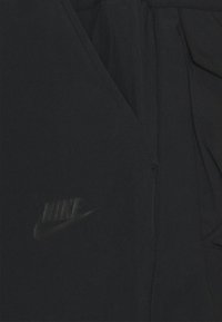 Černá bunda Nike s hladkým povrchem, zipovým zapínáním a vyvýšeným logem na levé straně hrudi. Celkově čistý a minimalistický design.