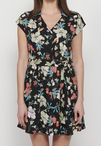 Vestido negro con flores que presenta mangas cortas, un escote en V, botones en la parte delantera y un cinturón anudado, adornado con flores coloridas y una falda plisada.