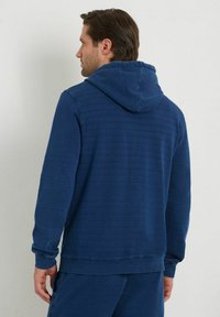 Felpa con cappuccio blu navy, dotata di cordino, maniche lunghe, polsini a costine e un tessuto morbido e strutturato. Presenta una vestibilità leggermente oversize.