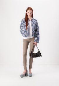 Sininen kuviollinen tilkkutakkimaiseen takki, valkoinen paita, beige slim-fit housut, harmaat kenkäalustat ja musta olkalaukku, jossa on soljet.
