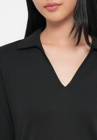 Czarny top w dekoltem w serek z kołnierzykiem, wykonany z prążkowanej tkaniny, prezentujący gładką fakturę i proste linie.