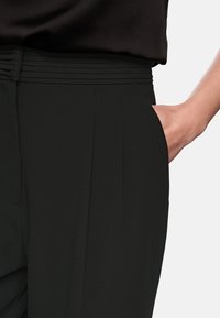 Schwarze Hose mit gerafftem Bund, seitlichen Taschen und glatter Textur. Das Design zeichnet sich durch klare Linien und eine taillierte Passform aus.