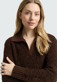 Bruine pullover trui met structuur, voorzien van een kraag en geribbelde manchetten, gemaakt van een zacht, pluizig materiaal en met een losse pasvorm.