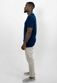 Marineblauwe T-shirt met korte mouwen, ontspannen pasvorm, gecombineerd met lichtbeige chino's en grijze instapschoenen, staande tegen een effen witte achtergrond.
