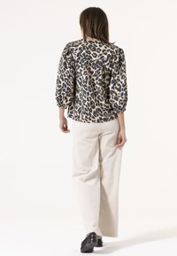Bluse mit Leopardenmuster und Puffärmeln, aus leichtem Stoff gefertigt, kombiniert mit weiten beige Hosen und schwarzen Schuhen.