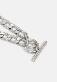 Colar de corrente de metal prateado com elos grandes, fecho em forma de toggle circular e um acabamento em barra reta. Superfície lisa e polida.