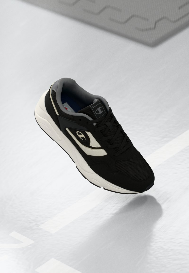Black athletic shoe with mesh and synthetic materials, featuring a white side accent, textured panels, and a solid rubber sole.