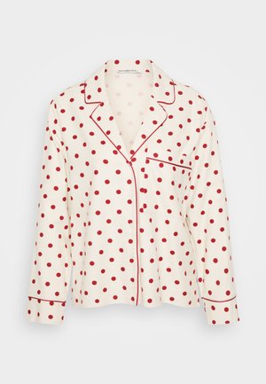 Weißes Langarmhemd mit roten Pünktchen und kontrastierenden roten Paspeln am Kragen und an der Tasche. Aus einem weichen Stoff gefertigt.