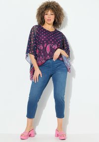 Elävä violetti puolipäiväinen yläosa, jossa on vaaleanpunaisia kukka- ja paisley-kuvioita, yhdistettynä sinisiin lyhyisiin farkkuihin ja vaaleanpunaisiin korkeakorkoisiin sandaaleihin.