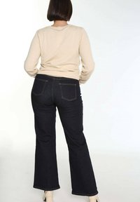 Beżowy sweter z długimi rękawami w połączeniu z ciemnoniebieskimi dzwonami. Dżinsy mają dwie tylne kieszenie i kontrastujące pomarańczowe szwy.