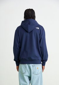 Navy blue hoodie with a drawstring and logo detail on the back, paired with light blue denim jeans. Soft fabric and relaxed fit.
