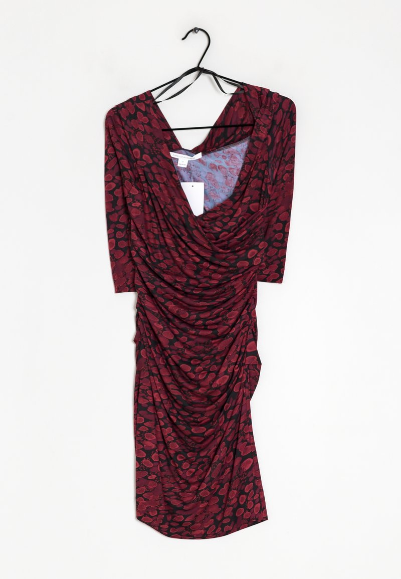Robe à motif floral rouge et noir avec un devant drapé et des manches courtes, fabriquée en tissu doux et extensible ; suspendue à un crochet noir.