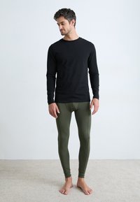 Svart langermet skjorte kombinert med olivengrønne leggings. Materialene ser myke ut med en tettsittende design, vist mot en nøytral bakgrunn.