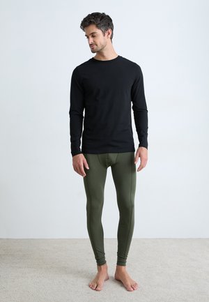 Schwarzes langärmeliges Shirt kombiniert mit olivgrünen Leggings. Die Materialien wirken weich und haben eine figurbetonte Passform, präsentiert vor einem neutralen Hintergrund.