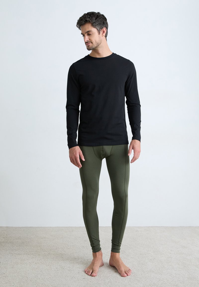 Svart langermet skjorte kombinert med olivengrønne leggings. Materialene ser myke ut med en tettsittende design, vist mot en nøytral bakgrunn.